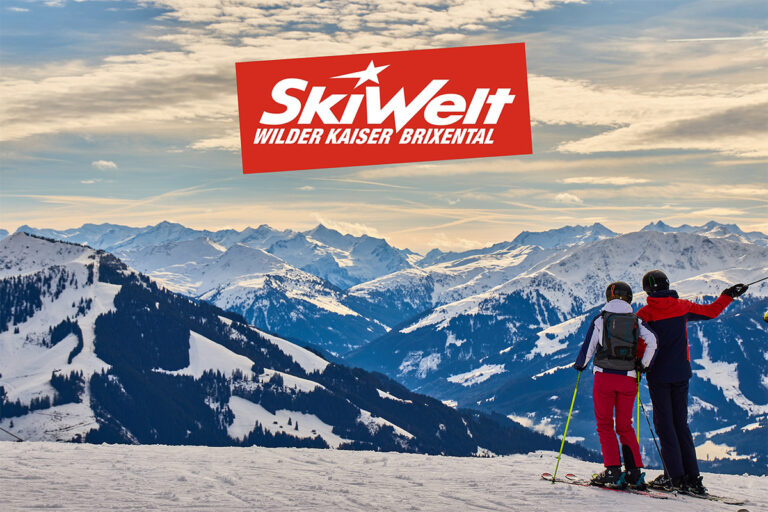 Zwei Skifahrer blicken von einer verschneiten Piste auf ein verschneites Bergpanorama der SkiWelt Wilder Kaiser - Brixental.